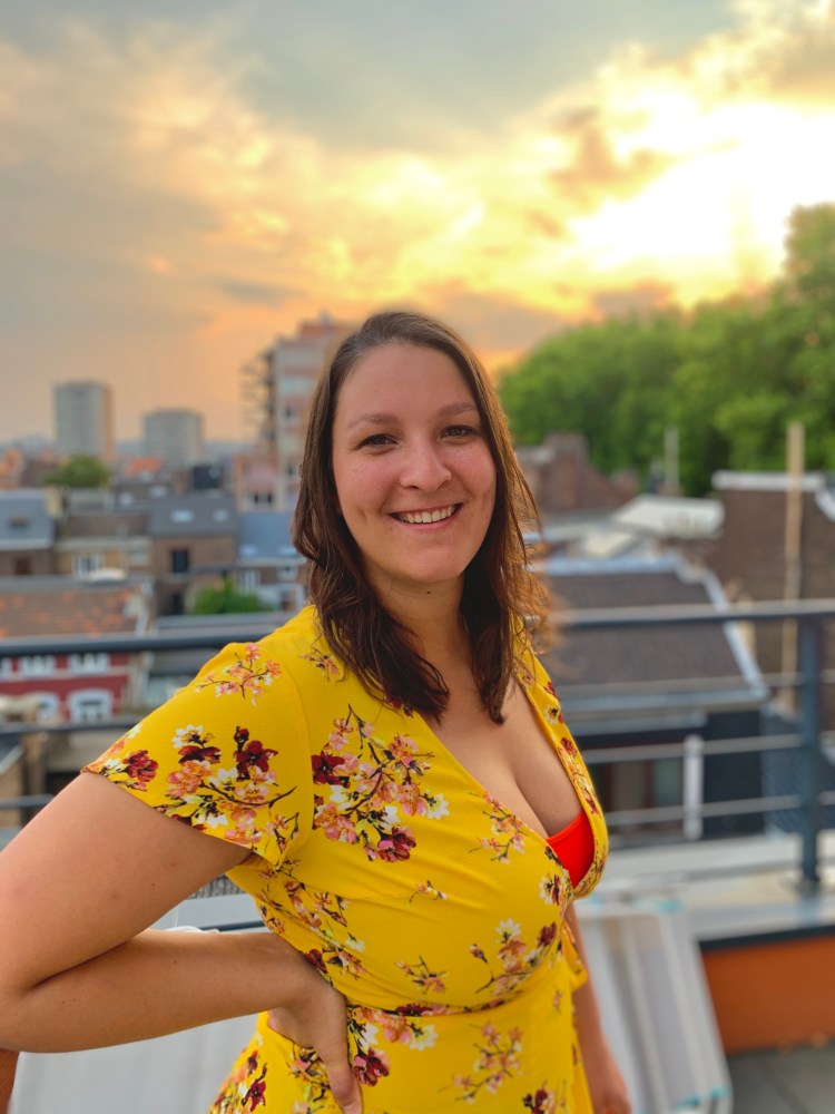 Photo d'Alison souriante dans une robe jaune et devant un coucher de soleil nuageux